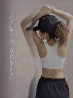 Woman in a white sports bra and black cap with arms raised