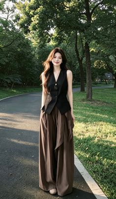 Woman with long hair wearing a black vest and wide leg pants in a park