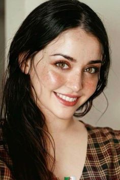 Woman with long dark hair and freckles smiling in a plaid shirt