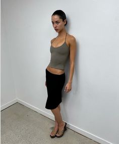 Woman in a halter top and black skirt leaning against a white wall