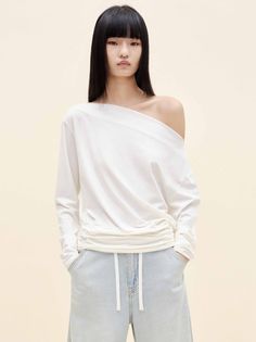 Woman with long black hair wearing an off-shoulder white top and light wash jeans