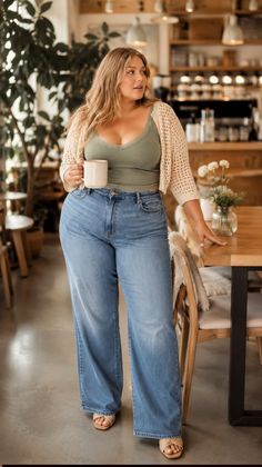 Woman with long hair in a cafe, wearing a green top and wide leg jeans