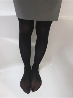 Person wearing black tights and a gray skirt standing against a white background