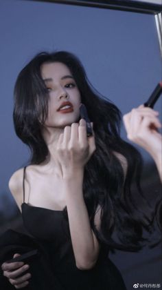 Woman with long black hair applying red lipstick in a mirror