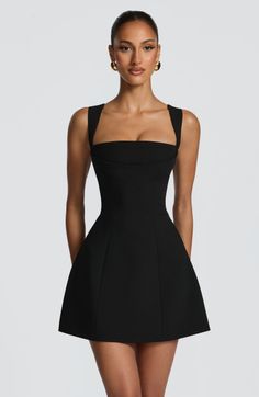 Woman in a black dress and gold earrings posing in a studio