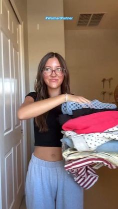Woman in a black crop top and sweatpants holding a stack of clothes