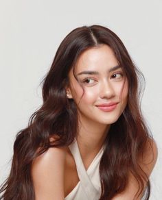 Woman with long wavy hair and a white top looking to the side