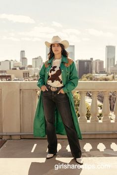 Woman in a cowboy hat and green trench coat on a rooftop with a cityscape background