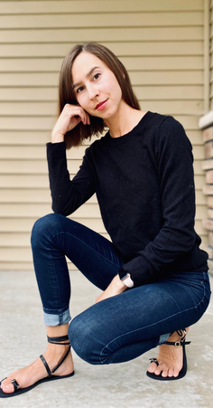 Woman in a black sweater and jeans crouching outdoors