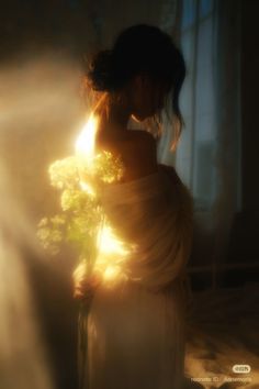 Woman with bun hair wrapped in white fabric, holding flowers in soft backlight
