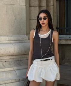 Woman with long hair wearing sunglasses, a tank top, and a white skirt outdoors