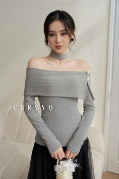 Woman in a gray off-shoulder top and choker holding a pearl bag indoors