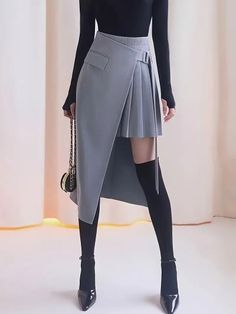 Person in an asymmetrical pleated skirt, black top, thigh-high socks, and high heels