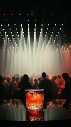 A cocktail glass with ice on a reflective surface in a dark nightclub with spotlights