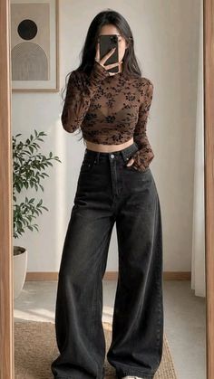 Woman in a sheer floral crop top and wide leg jeans taking a mirror selfie