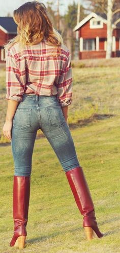 Woman in a plaid shirt, skinny jeans, and red boots standing in a grassy field