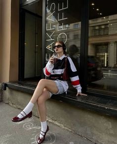 Woman in a long sleeve shirt and denim shorts sitting on a ledge outdoors
