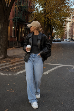 Woman in a baseball cap and leather jacket walking on a street with autumn leaves