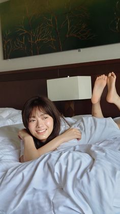 Woman with long hair smiling while lying on a bed with white sheets