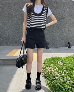 Person in a striped vest and black shorts holding a black handbag outdoors