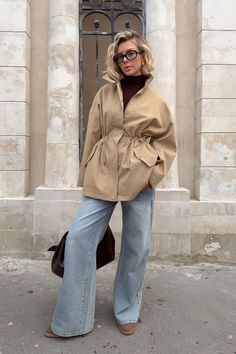 Woman with short blonde hair and glasses wearing a beige jacket and wide leg jeans