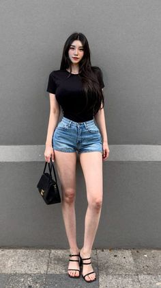 Woman with long black hair wearing a black t-shirt and denim shorts outdoors