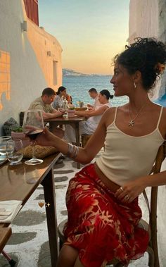 Woman in a red skirt and white top dining outdoors by the sea at sunset