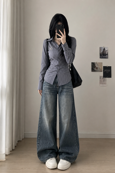 Person with long black hair wearing a striped shirt and wide leg jeans indoors