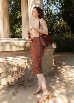 Woman in a polka dot skirt and gold sandals holding sunglasses outdoors