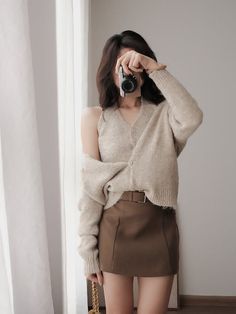 Woman in a cardigan and mini skirt holding a camera indoors