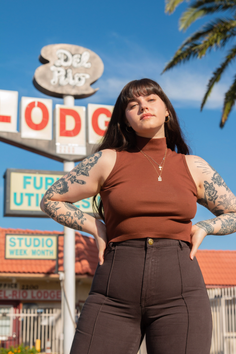 Woman with long hair and tattoos posing outdoors in front of a hotel sign
