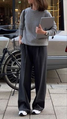 Person in a grey sweater and black pants holding a tablet outdoors