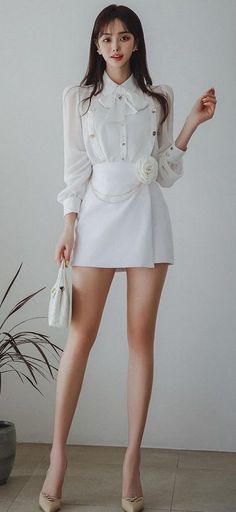 Woman in a white blouse and mini skirt holding a white handbag indoors