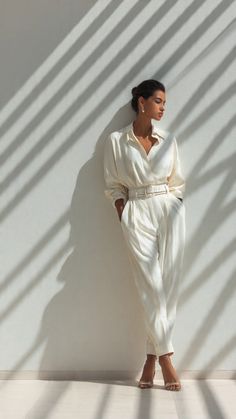 Woman in a white jumpsuit leaning against a wall with shadow stripes