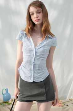Woman with long hair and freckles wearing a striped shirt and short skirt indoors