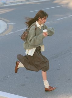 Woman in a sweater and skirt running on a street with a coffee cup