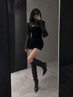 Woman in a black dress and thigh-high boots posing in a mirror
