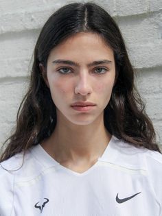 Woman with long dark hair wearing a white shirt, looking directly at the camera
