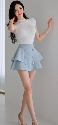 Woman with long black hair wearing a white top and blue mini skirt indoors