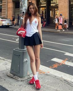 Woman in a white top and black pleated skirt holding a camera on a city street