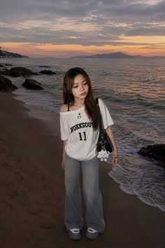 Woman in an off-shoulder top and jeans on a beach at sunset