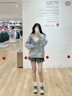 Woman in a grey hoodie and pleated skirt taking a mirror selfie in a clothing store