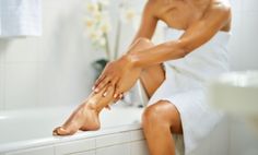 Person in a white towel applying lotion to their leg in a bathroom
