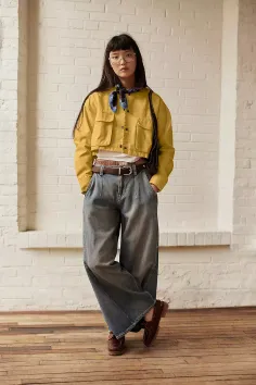 Woman in a yellow jacket, wide leg jeans, and a bandana standing indoors