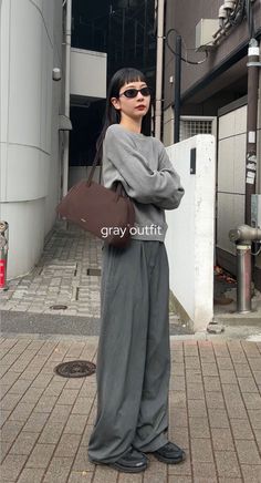 Woman in a gray outfit and sunglasses standing on a street