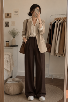 Woman in a blazer and wide leg pants taking a mirror selfie indoors