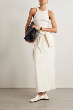 Woman in a white tank top and long skirt holding a black clutch bag