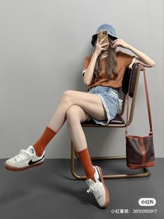 Person in a denim bucket hat and shorts sitting on a chair, taking a mirror selfie