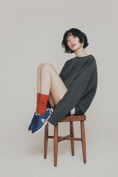 Woman with short black hair wearing an oversized sweatshirt and red socks, sitting on a stool