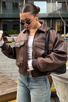 Woman in a brown leather jacket and sunglasses holding a cup outdoors